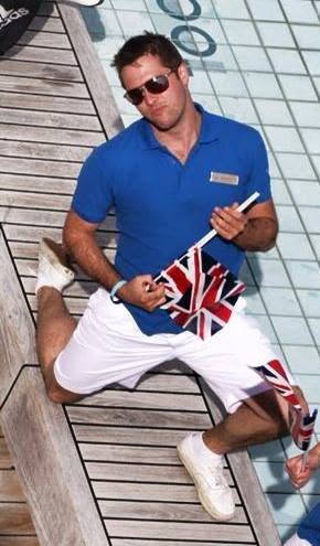 Alexander Percival in a blue Activity Host shirt and sunglasses, holding Union Jack flags by a ship’s pool